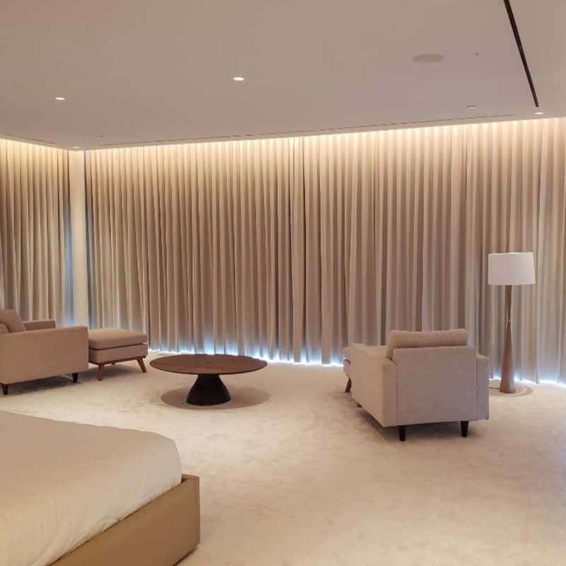 An elegant and minimalist living room with floor-to-ceiling wave-patterned drapery, complemented by soft lighting, a central round coffee table, and two plush armchairs flanking a matching sofa.